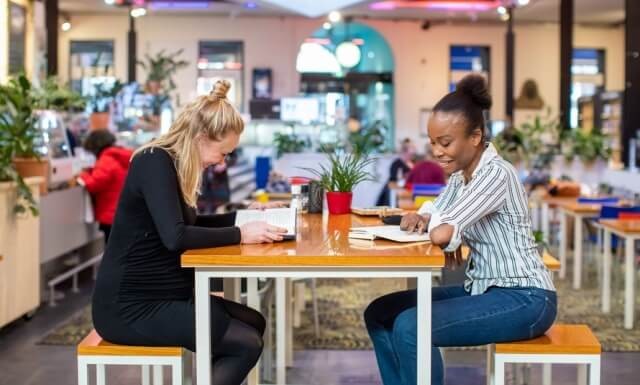 Twee vrouwen lezen aan tafel in brasserie